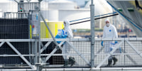 Specialist workers in full PPE carry boxes containing hazardous waste.