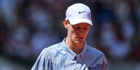 Jannik Sinner looks down while walking outside on the tennis court