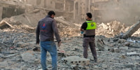 Civil defense workers inspect rubble from destroyed buildings outside