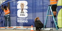 Workers affix FIFA World Cup 2026 logos and signage on a fence outside of SoFi Stadium