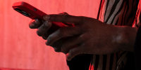Image: A man holds a smartphone while standing near a wall with red neon lighting
