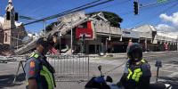 A severely damaged commercial building behind two police officers.