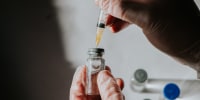 A healthcare professional uses a syringe to draw liquid medicine from a vial.