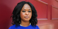 Janeese Lewis George stands for a portrait in front of a red background