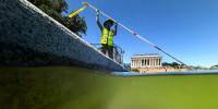 A U.S. National Park Service employee uses a vacuum pump to clean algae off the bottom of the newly repainted Lincoln Memorial Reflecting Pool