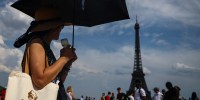 A woman protects herself from the sun under an umbrella on the Trocadero square near the Eiffel Tower as temperatures rise in Paris during a second heatwave affecting a large part of France, June 20, 2026. 