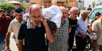 Mourners carry a body covered in white tarp outside