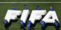 10 men in blue t-shirts carrying giant white letters spelling FIFA