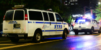 Two NYPD cars drive on the street at night