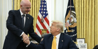 Donald Trump, seated at his Oval Office desk, shaking the hand of Gianni Infantino who stands next to him.