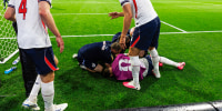 Declan Rice, left, and Dan Burn stand around Jordan Henderson who is crumpled on the ground on the soccer field