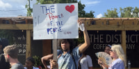 A young man holding a sign reading THE POWER OF THE PEOPLE at a small protest.