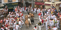 People dressed in white with red neckerchiefs run from bulls on the brick streets of Pamplona.