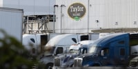 Several semi-trucks parked in front of a warehouse with the Taylor Farms logo on its facade.