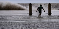 A boy frolics in the water near a lake as a wave crashes