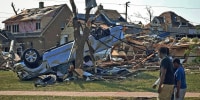 People walk past damaged homes in Menasha, Wis., on July 28, 2026, the day after a tornado tore through the area.