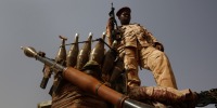 A Sudanese soldier from the Rapid Support Forces stands on a vehicle while holding a weapon.