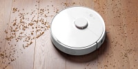 Image: Smart robot vacuum cleaner removes scattered debris from the laminate floor. The concept of a smart home, wireless cleaning of any surfaces