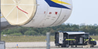 Police forensic technicians prepare to deploy an explosive-disposal robot near an aircraft.