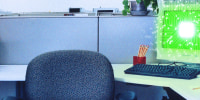 An empty office chair and a computer screen illuminated with digital, AI chip texture in a cubicle.