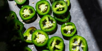 Fresh cut jalapeño slices laid on a gray surface
