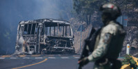 A soldier stands guard by a charred vehicle.