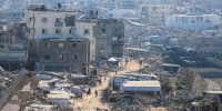 A high-angle view shows makeshift shelters and tents among damaged buildings and rubble.