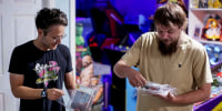 Two men stand while holding video games cases on their hands.
