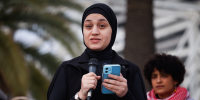 Wissam Hamada speaks into a microphone while standing and hold a cellphone in the other hand