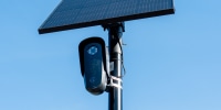 A Flock camera is mounted on a pole underneath a solar power panel