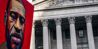 A poster of a painting of George Floyd is held up near a building exterior outside