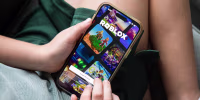 A child holds a smartphone displaying the Roblox app login page