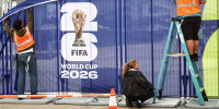 Workers affix FIFA World Cup 2026 logos and signage on a fence outside of SoFi Stadium