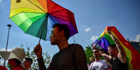 A person holds an umbrella in the colors of a Pride flag.