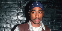 Tupac Shakur stands up again a brick wall painted black