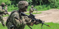 Luke Lem in his army uniform carries a gun while walking in a field
