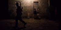 A guerrilla member walks in front of a house as a child appears to walk-in.
