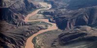 An aerial view of the Grand Canyon landscape with the Colorado River winding through it.
