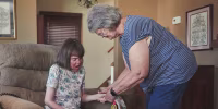 Image: Nancy Enstrom holding her daughter Anna's hand while assisting her at home.