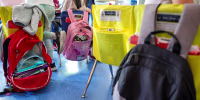 Student backpacks hang on the backs of classroom chairs.