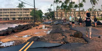 People walk past a damaged road
