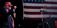 Donald Trump raises his fists while dancing on stage during an evening rally. 