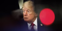 President Trump is partially obscured by a blurred foreground with a bright red dot.