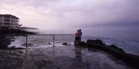 A couple observing a purple sunset over a cloudy sky on the Hawaiian coastline.