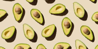 Pattern of fresh ripe green avocado fruit halves on beige background. Healthy food, diet and detox concept. Flat lay, top view