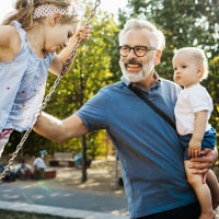 Grandfather Having Fun With Grandchildren On Swings