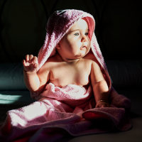 Cute baby girl in towel looking away while sitting on bed at home