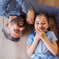Top view of mature father and small daughter lying on floor indoors at home.