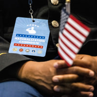 A person seated, focus is on a badge they're wearing that reads "naturalization candidate" as they hold an American flag