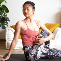 Young Asian woman doing seated spinal twist at home living room.